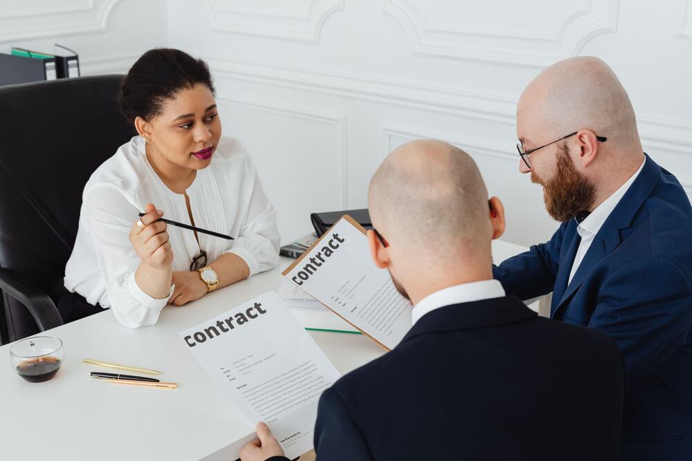 Three professionals reviewing a contract around a desk (representative stock photo)